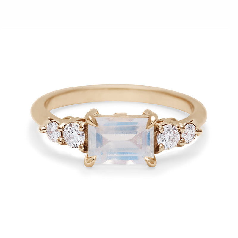A ring with an emerald cut and shaped rainbow moonstone center stone with two round white diamonds on either side set in yellow gold., Yellow Gold