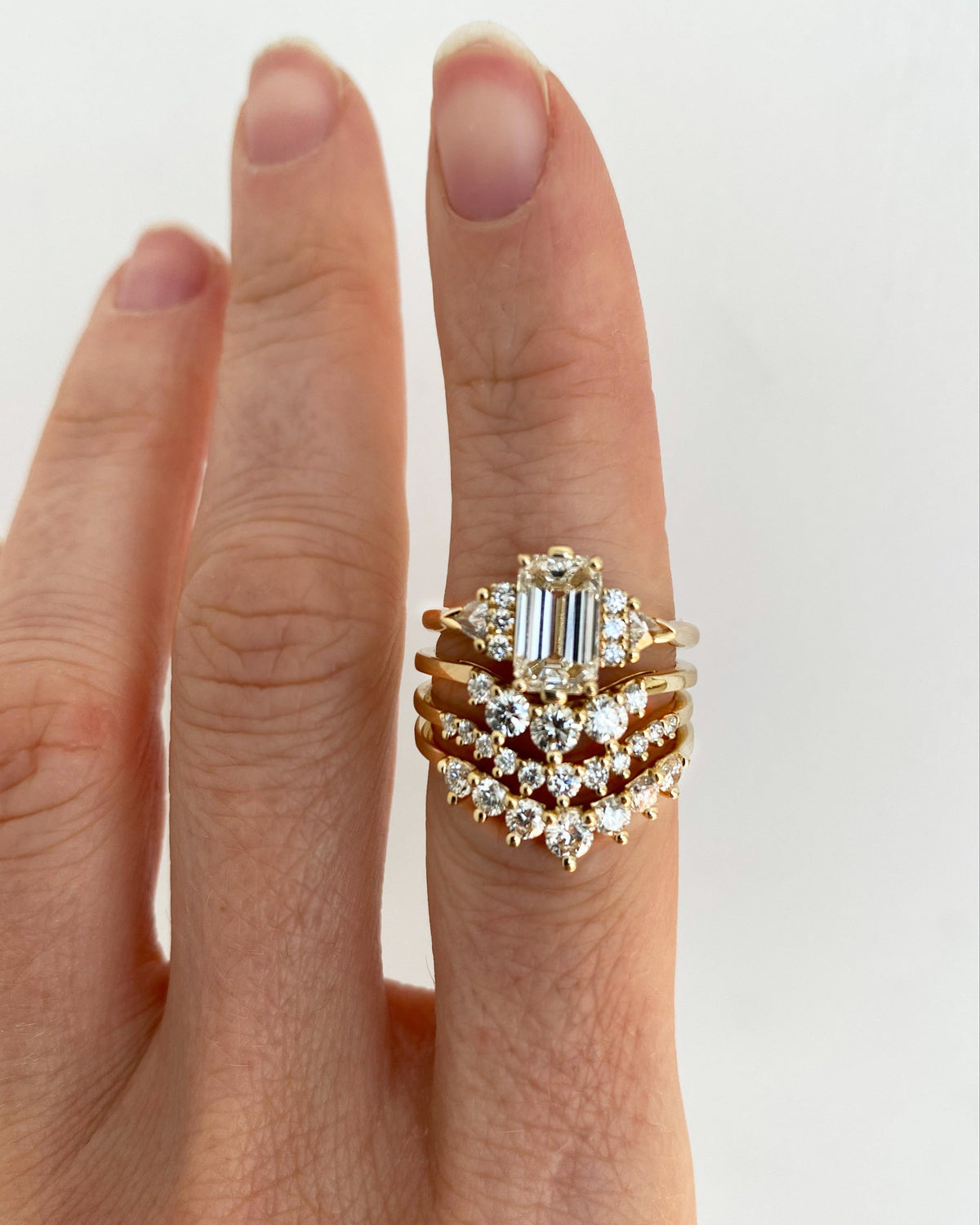 An white emerald cut diamond engagement ring paired with three yellow gold white diamond stacking bands on a finger