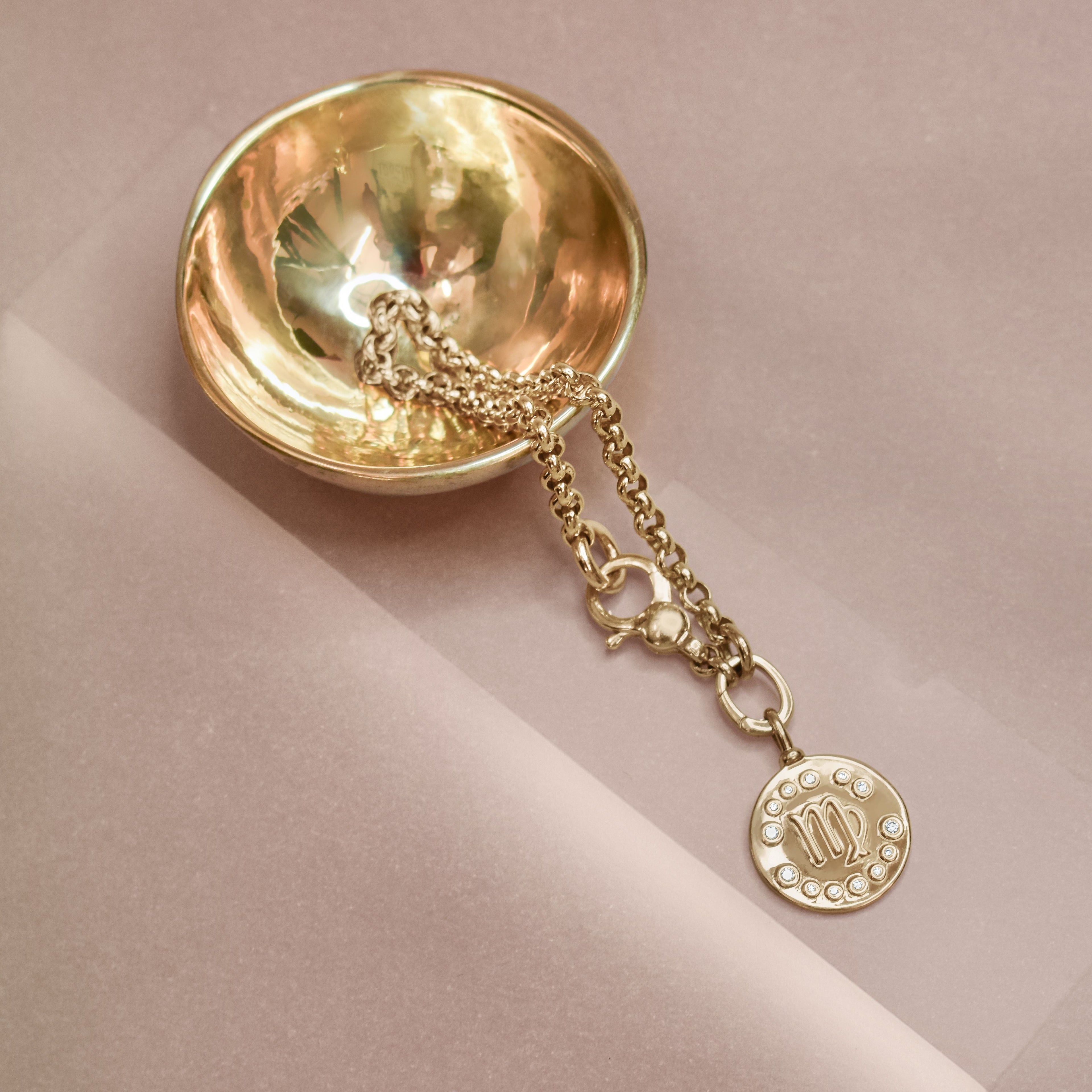 gold rolo chain with a gold zodiac charm in a brass bowl. 