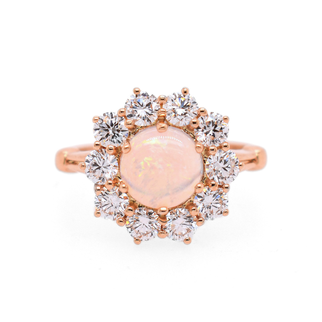 A ring featuring a cabochon fire opal center stone encircled in 3mm white round diamonds to create a flower appearance set in rose gold. 