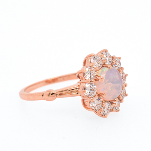 3/4 angle of a ring featuring a cabochon fire opal center stone encircled in 3mm white round diamonds to create a flower appearance set in rose gold. 