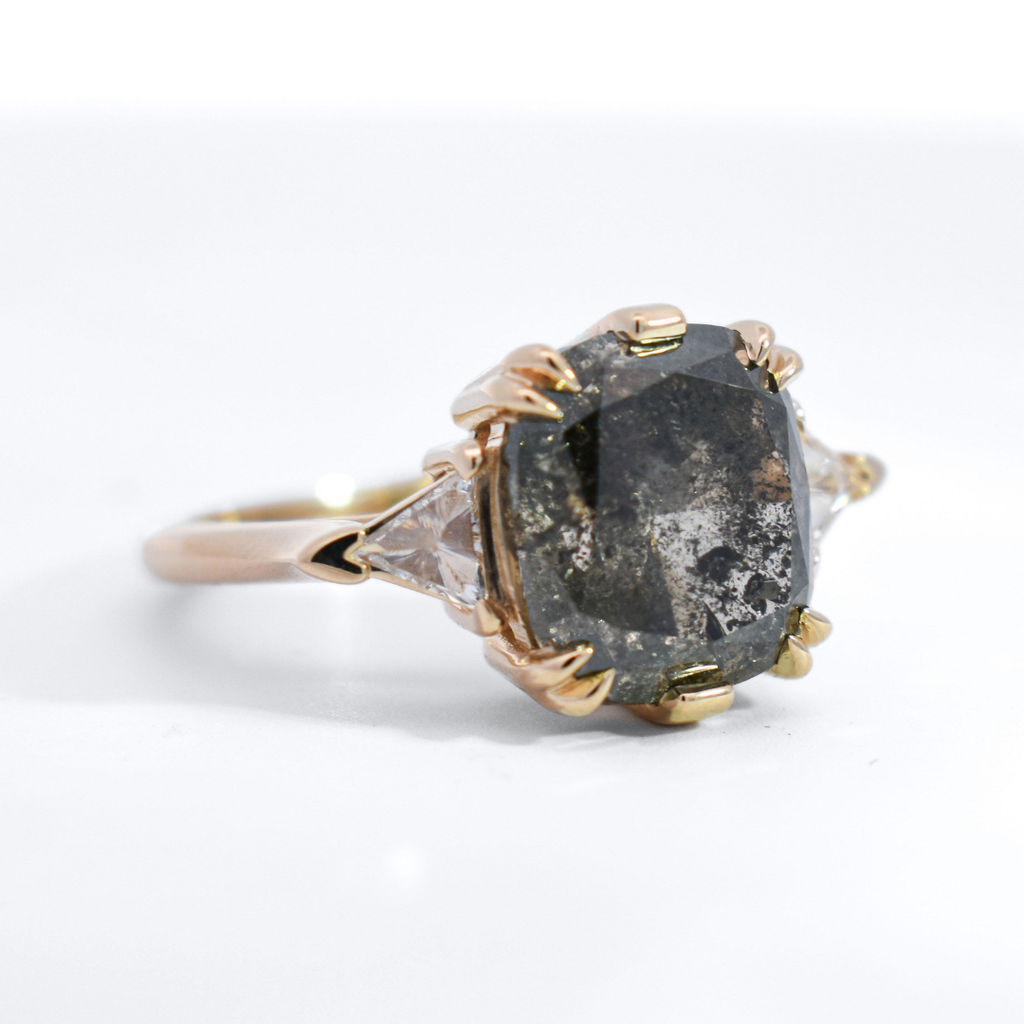 3/4 angle of a three stone ring featuring a black oval rose cut diamond and white trillion diamond side stones set in yellow gold. 