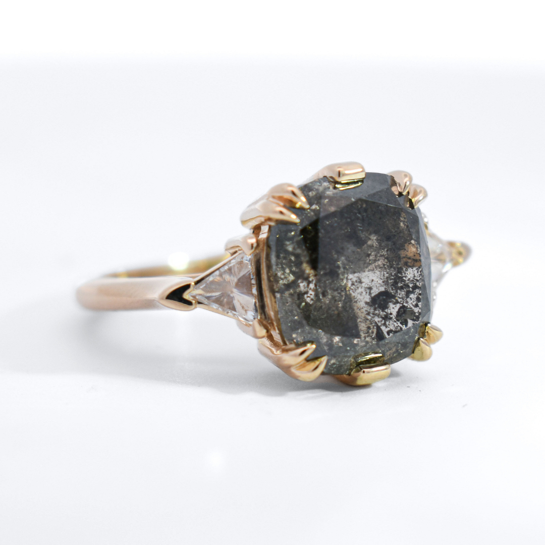 3/4 angle of a three stone ring featuring a black oval rose cut diamond and white trillion diamond side stones set in yellow gold. 