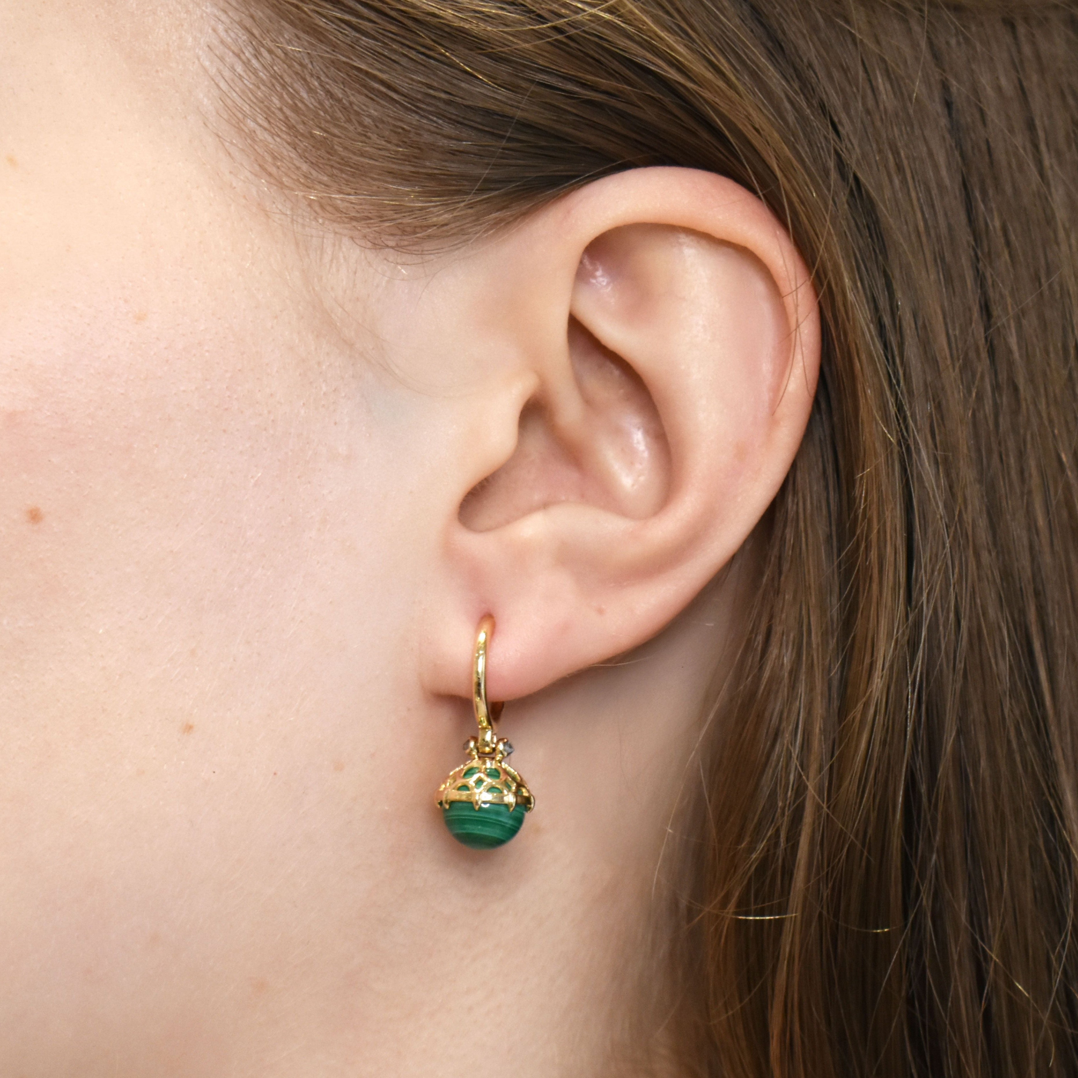 A malachite drop earring set in yellow gold in an ear. 