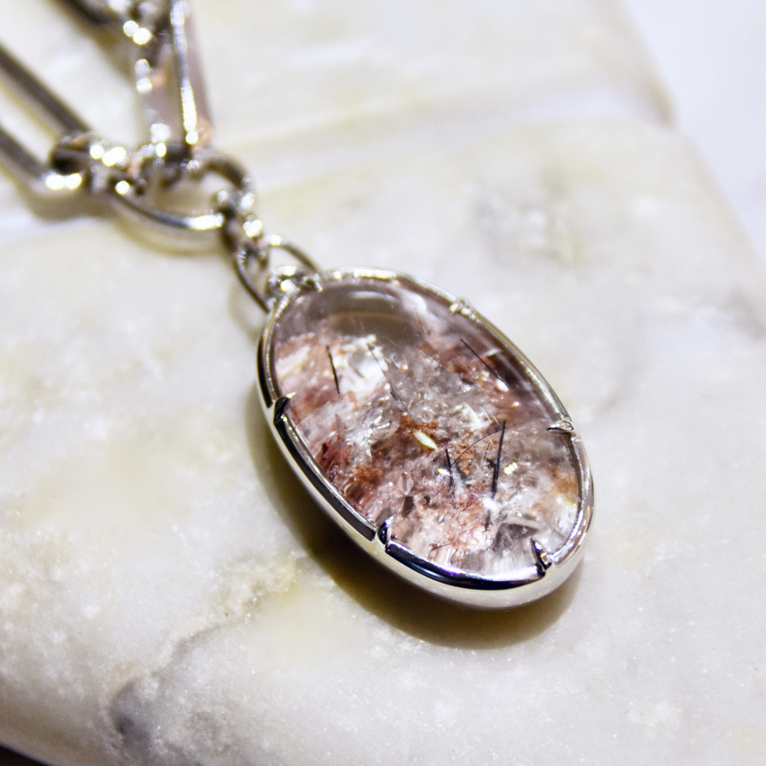 An oval cabochon garden quartz pendant set in white gold on a white gold chain placed on a white marbled stone surface. 