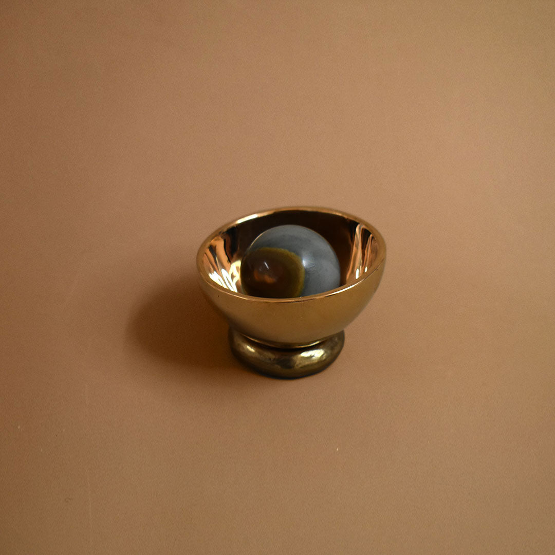 Bronze decorative bowl object with a jasper gemstone inside the bowl on a beige background