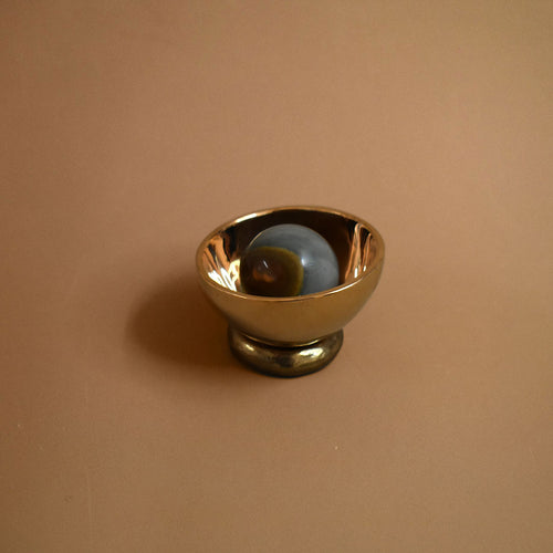 Bronze decorative bowl object with a jasper gemstone inside the bowl on a beige background
