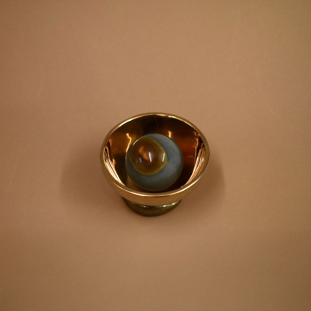 Bronze decorative bowl object with a jasper gemstone inside the bowl on a beige background