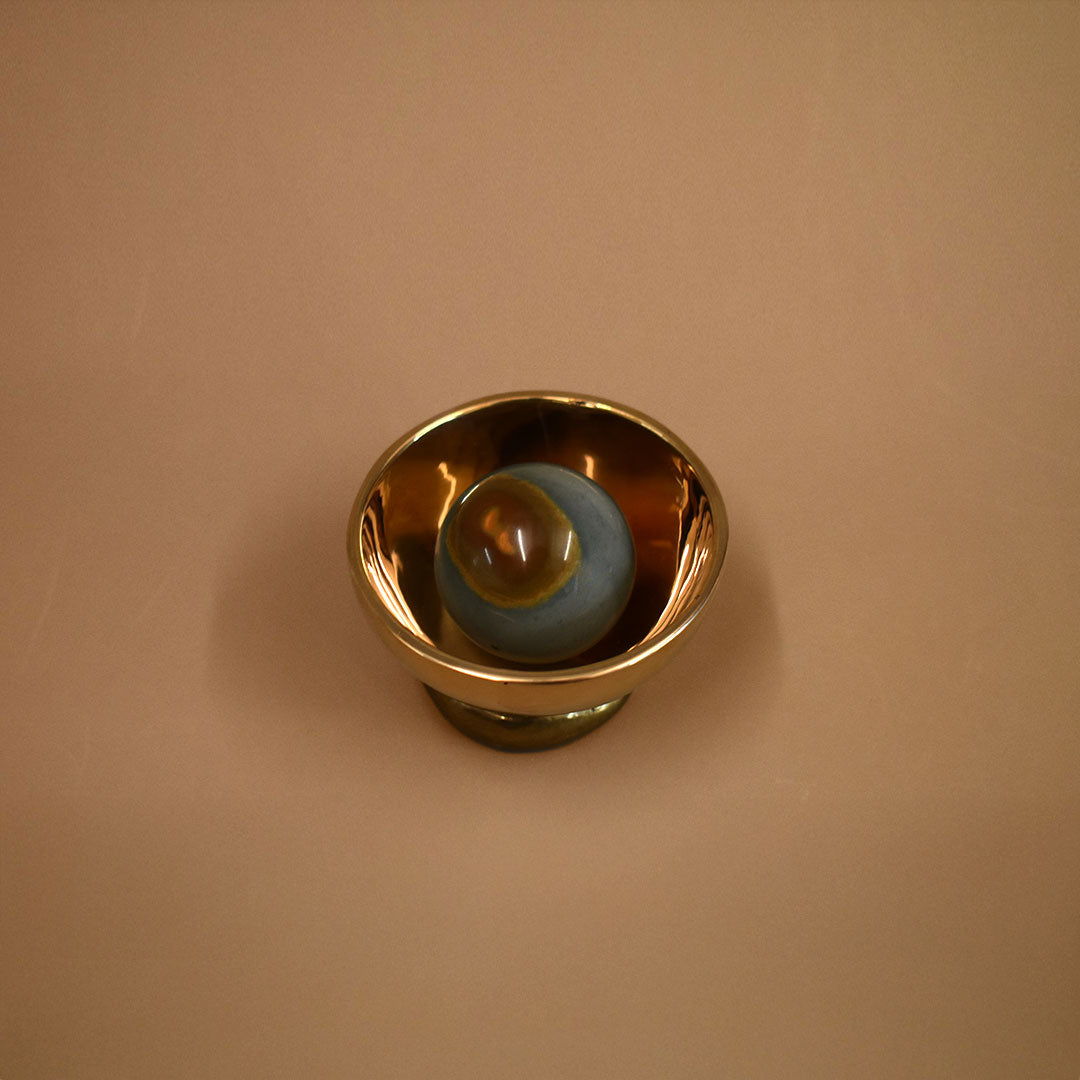 Bronze decorative bowl object with a jasper gemstone inside the bowl on a beige background