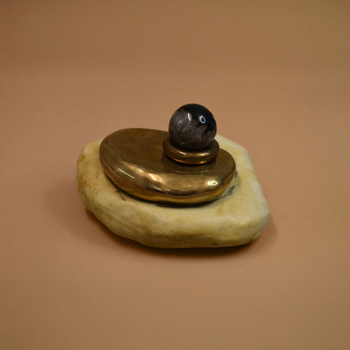 Decorative object with a gold brass base, black agate gemstome sphere, and beige porcelain stone on a brown background
