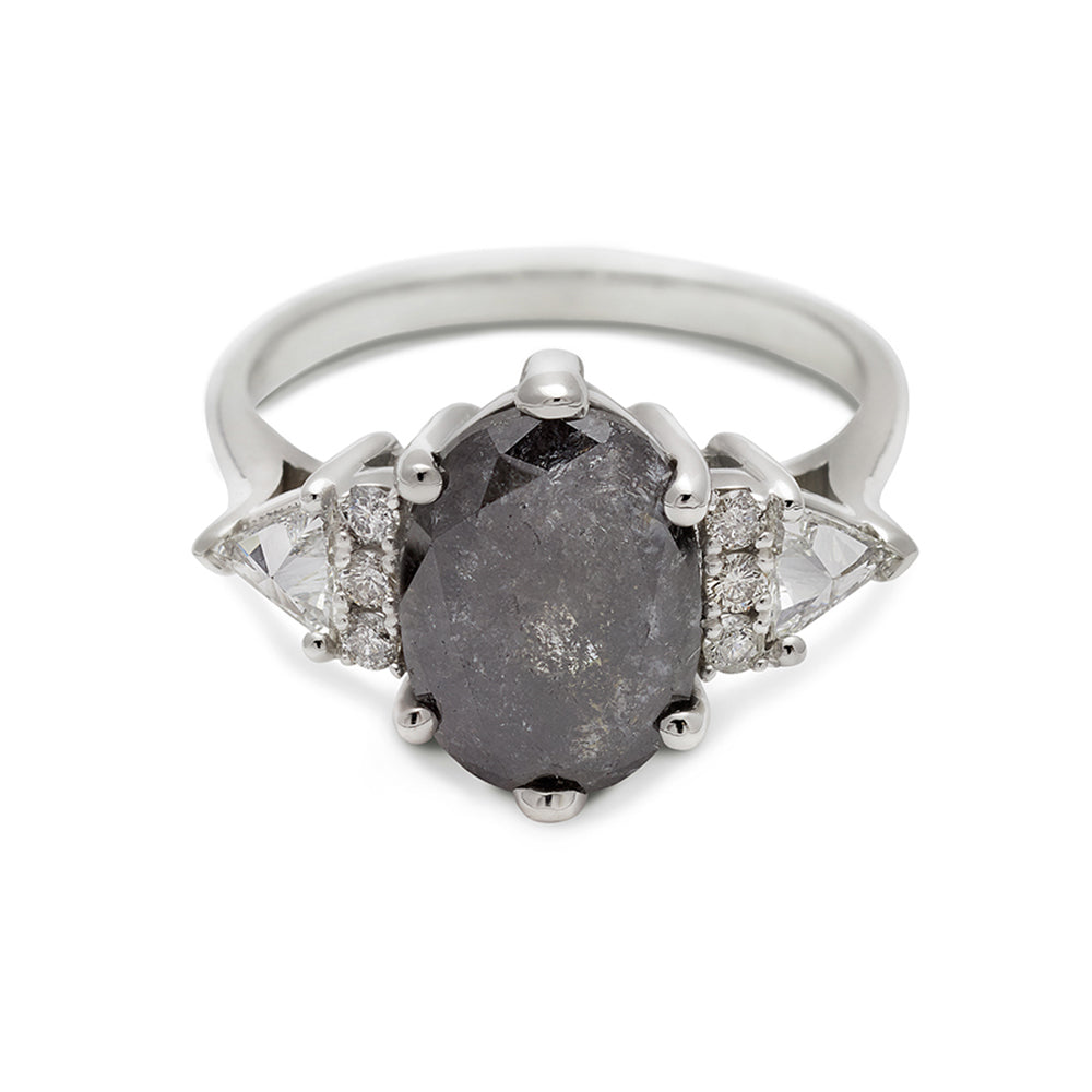 An oval shaped 2.00ct grey diamond center stone ring with three round white diamonds on either and two white diamond trillions on the outer edges of each side set in white gold.