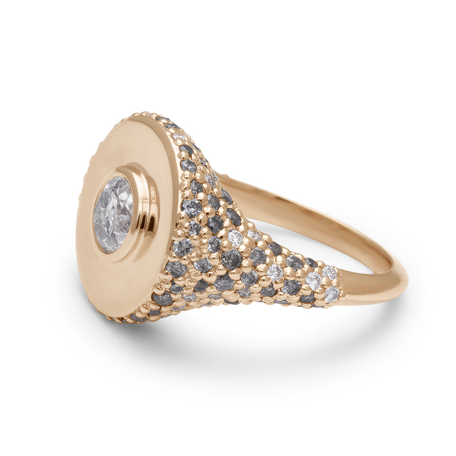 Angled view of a round grey diamond bezel set in a signet style ring with white and grey diamond pave down the sides of the band set in yellow gold.
