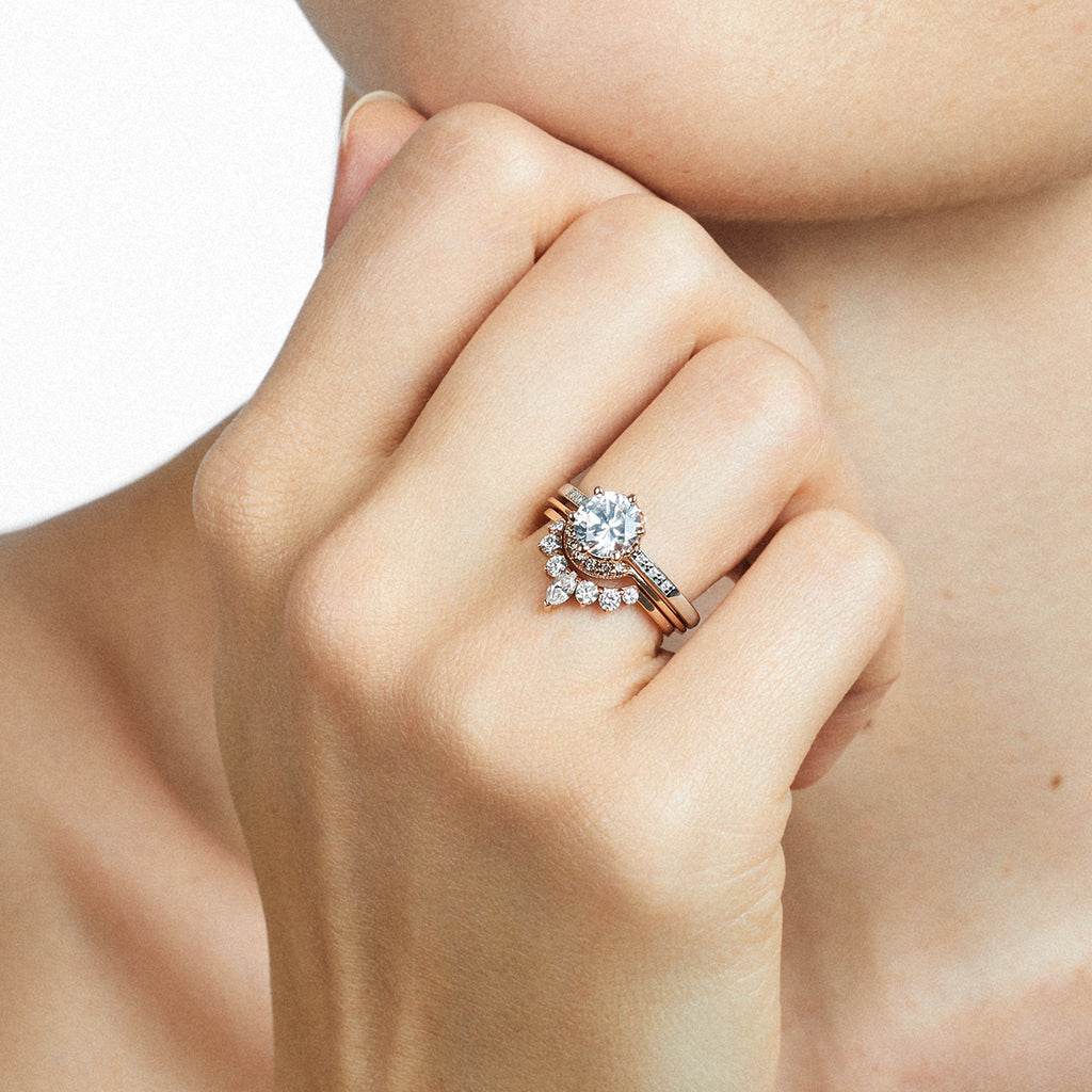 A hand wearing a band and engagement ring with marquise shaped white diamonds with round white diamond set in yellow gold and a round solitaire engagement ring., Available in Yellow Gold, Rose Gold, White Gold.