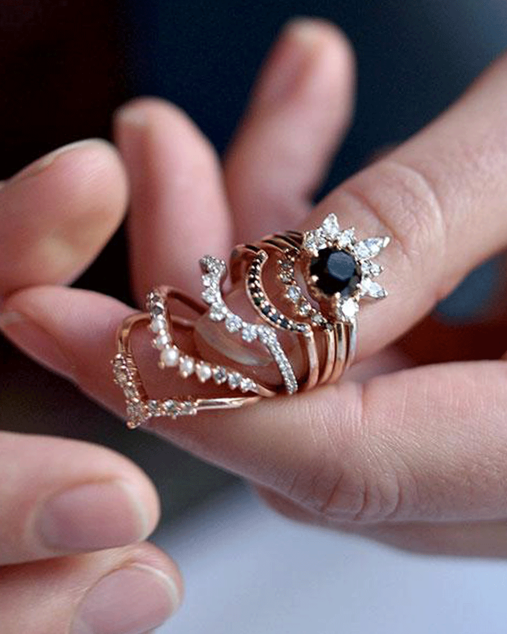 A paire of hands holding an engagement ring with various wedding bands