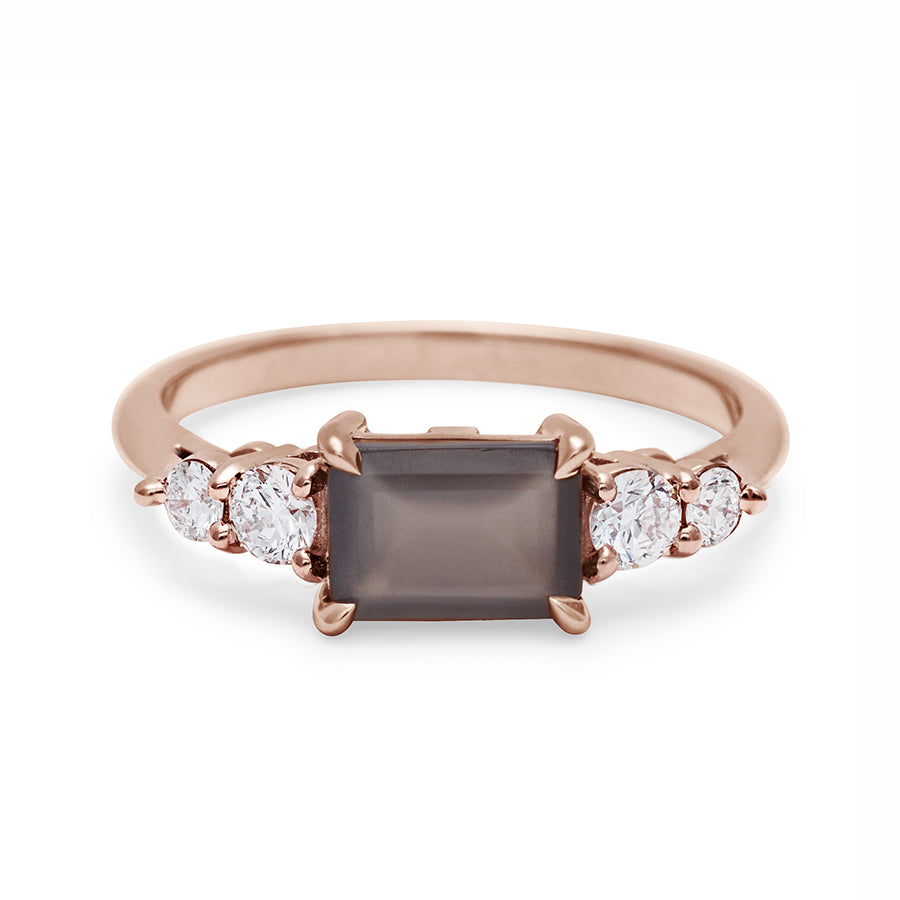 A ring with an emerald shaped grey moonstone center stone with two round white diamonds on either side set in rose gold., Rose Gold