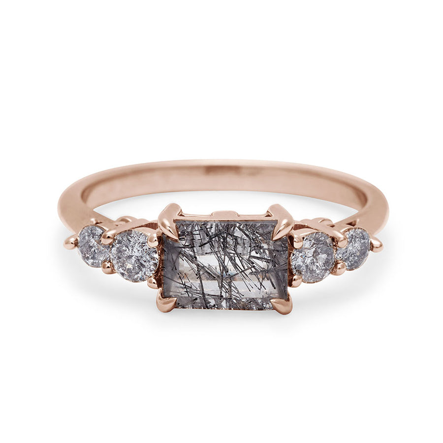A ring with an emerald shaped black rutilated quartz center stone with two round grey diamonds on either side set in rose gold., Rose Gold
