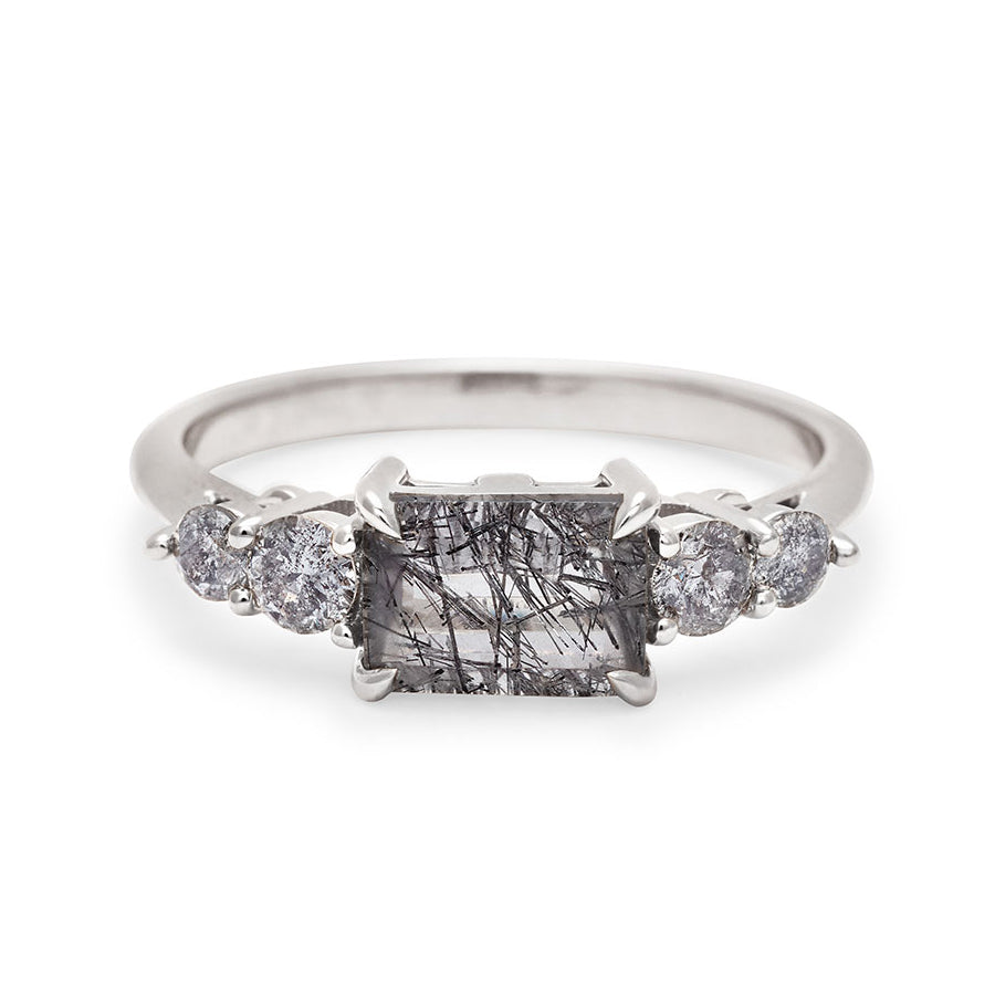 A ring with an emerald shaped black rutilated quartz center stone with two round grey diamonds on either side set in white gold., White Gold