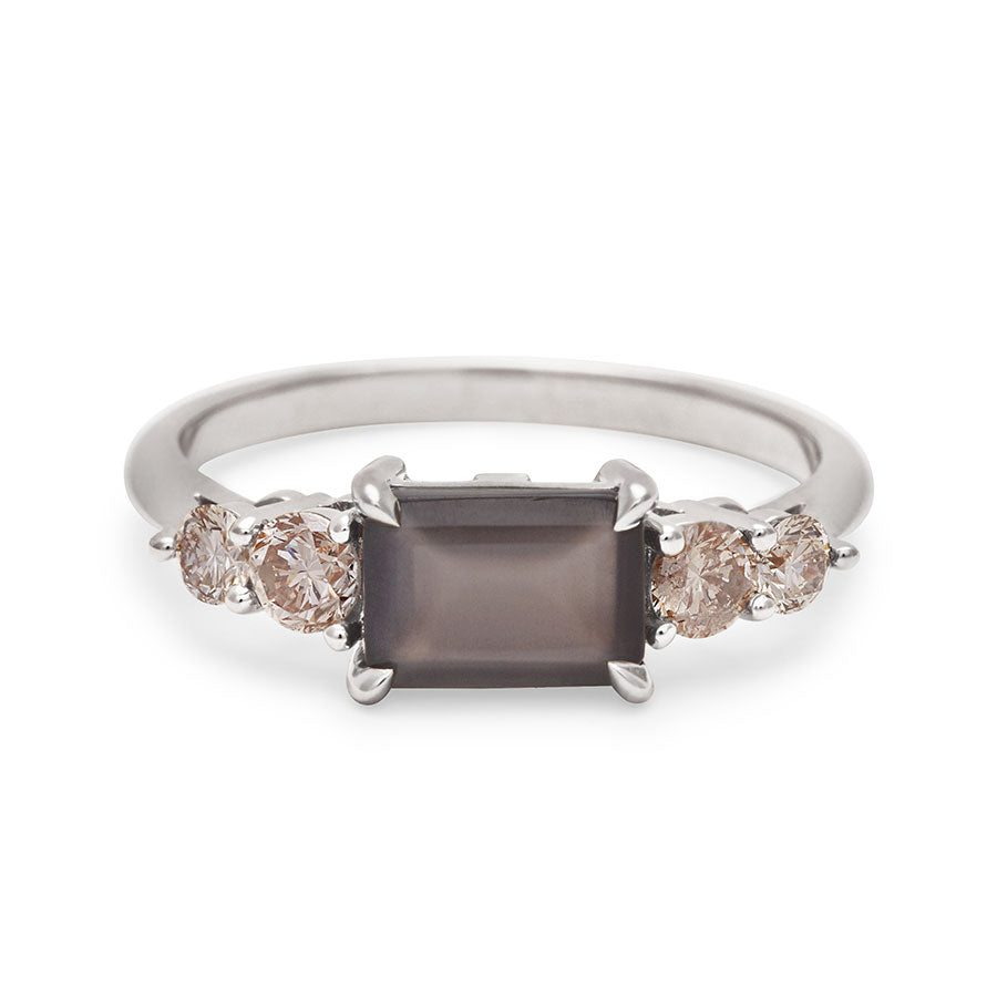 A ring with an emerald shaped grey moonstone center stone with two round champagne diamonds on either side set in white gold., White Gold
