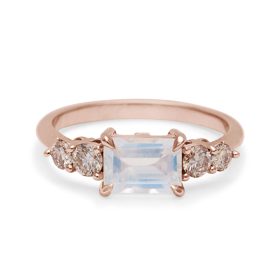 A ring with an emerald cut and shaped rainbow moonstone center stone with two round champagne diamonds on either side set in rose gold., Rose Gold