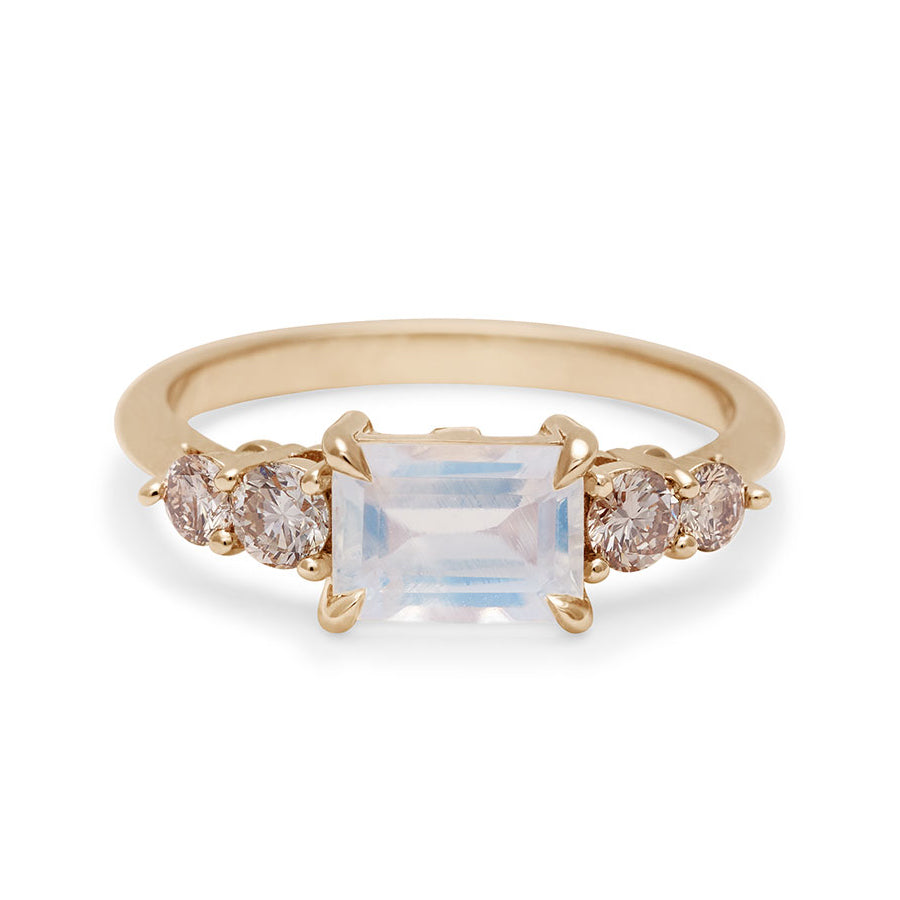 A ring with an emerald cut and shaped rainbow moonstone center stone with two round champagne diamonds on either side set in yellow gold., Yellow Gold