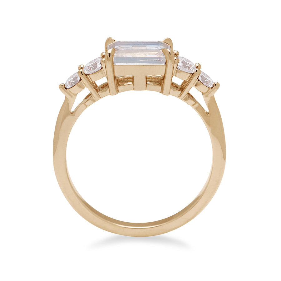 Side view of a ring with an emerald cut and shaped rainbow moonstone center stone with two round white diamonds on either side set in yellow gold.