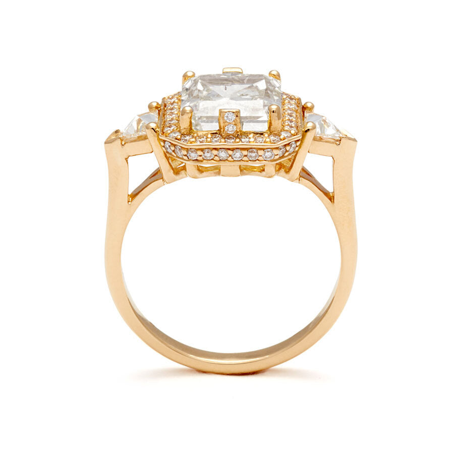 A radiant cut lab white diamond encircled by a white diamond halo and two white lab trillion diamond side stones set in a yellow gold ring on a white background 