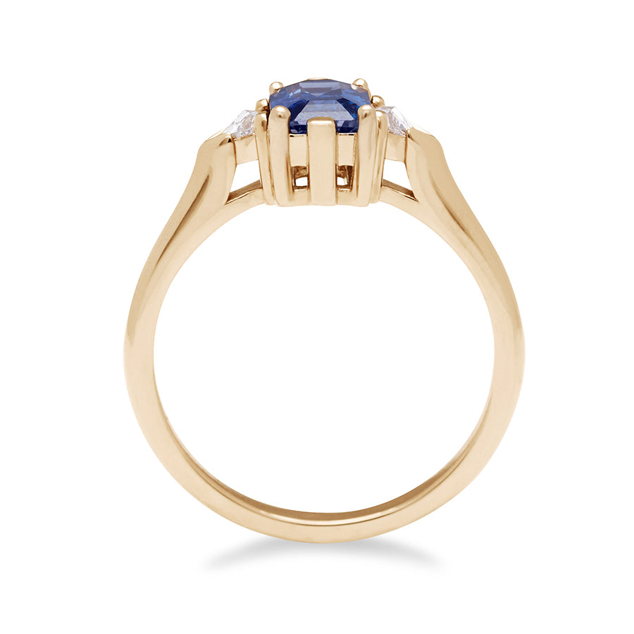 Side view of a three stone engagement ring with an emerald cut and emerald shape 7x5mm blue sapphire center stone with two white diamond trillion side stones set in yellow gold., Yellow Gold