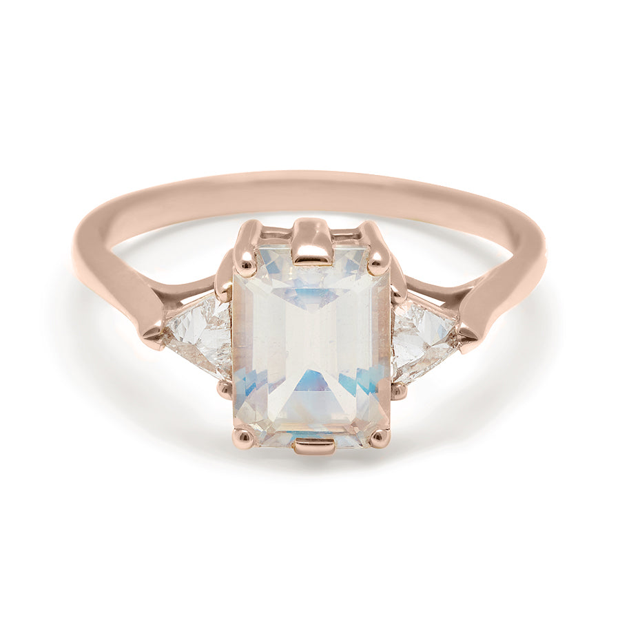 A three stone engagement ring with an emerald cut and emerald shape 8x6mm rainbow moonstone center stone with two white diamond trillion side stones set in rose gold., Rose Gold