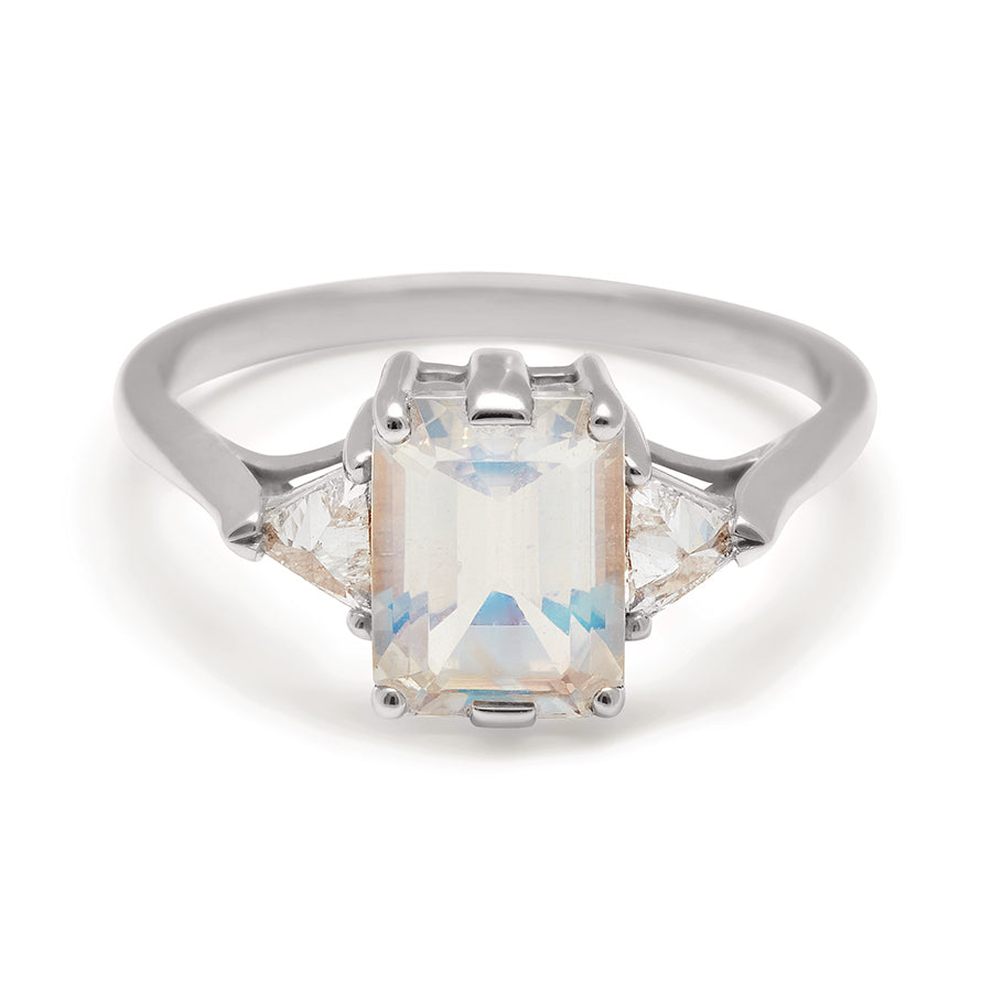 A three stone engagement ring with an emerald cut and emerald shape 8x6mm rainbow moonstone center stone with two white diamond trillion side stones set in white gold., White Gold
