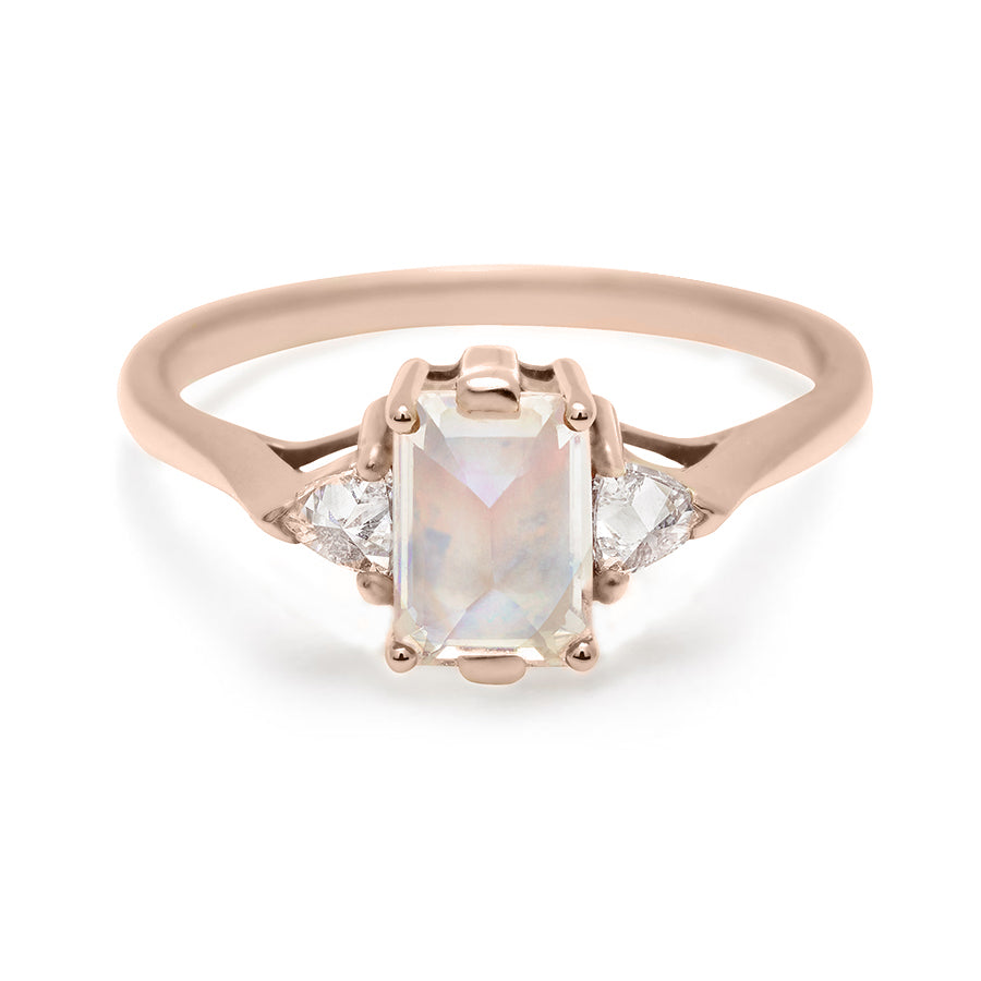 A three stone engagement ring with an emerald cut and emerald shape 7x5mm rainbow moonstone center stone with two white diamond trillion side stones set in rose gold., Rose Gold