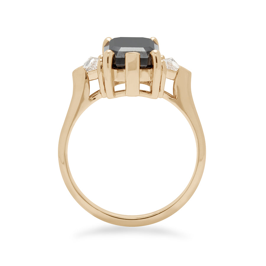 Side view of a three stone engagement ring with an emerald shape black diamond center stone with two white diamond trillion side stones set in yellow gold., Yellow Gold