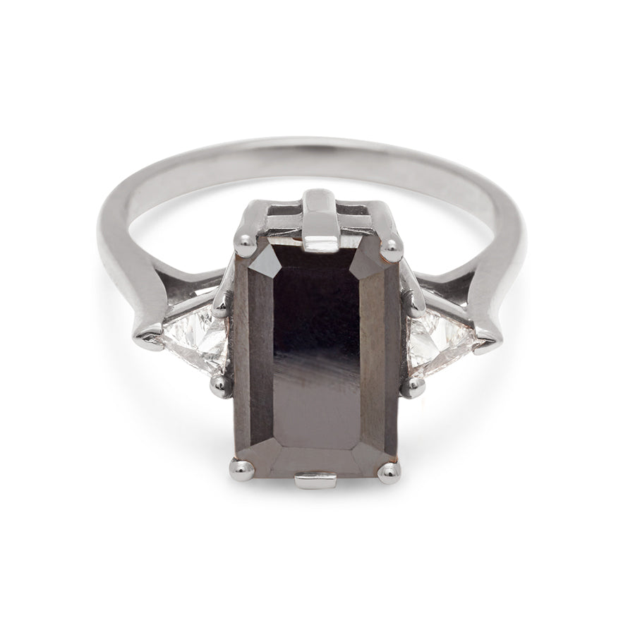 A three stone engagement ring with an emerald shape black diamond center stone with two white diamond trillion side stones set in white gold., White Gold