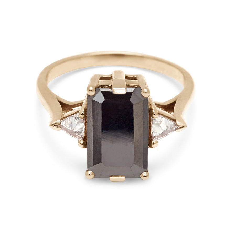 A three stone engagement ring with an emerald shape black diamond center stone with two white diamond trillion side stones set in yellow gold., Yellow Gold