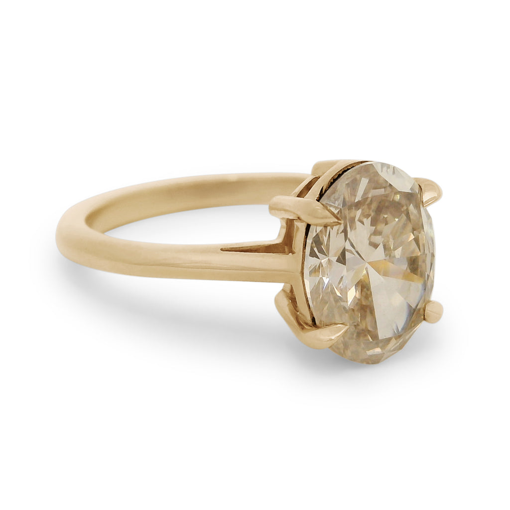 Side profile of a champagne oval diamond engagement ring set in yellow gold on a white background