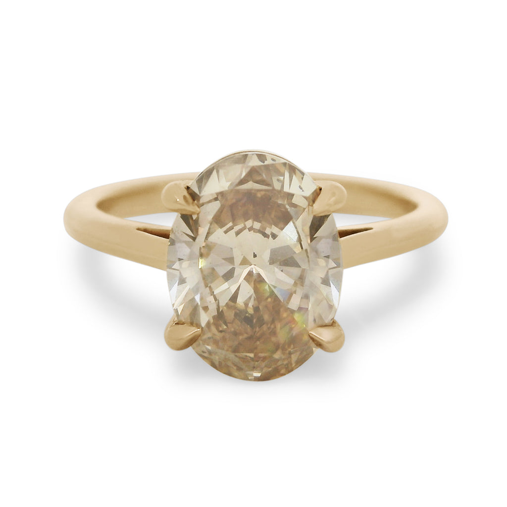 A champagne oval diamond engagement ring set in yellow gold on a white background