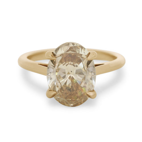 A champagne oval diamond engagement ring set in yellow gold on a white background