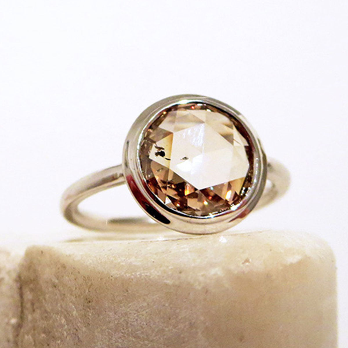 A round rose cut bezel set champagne diamond set in white gold on a white stone.