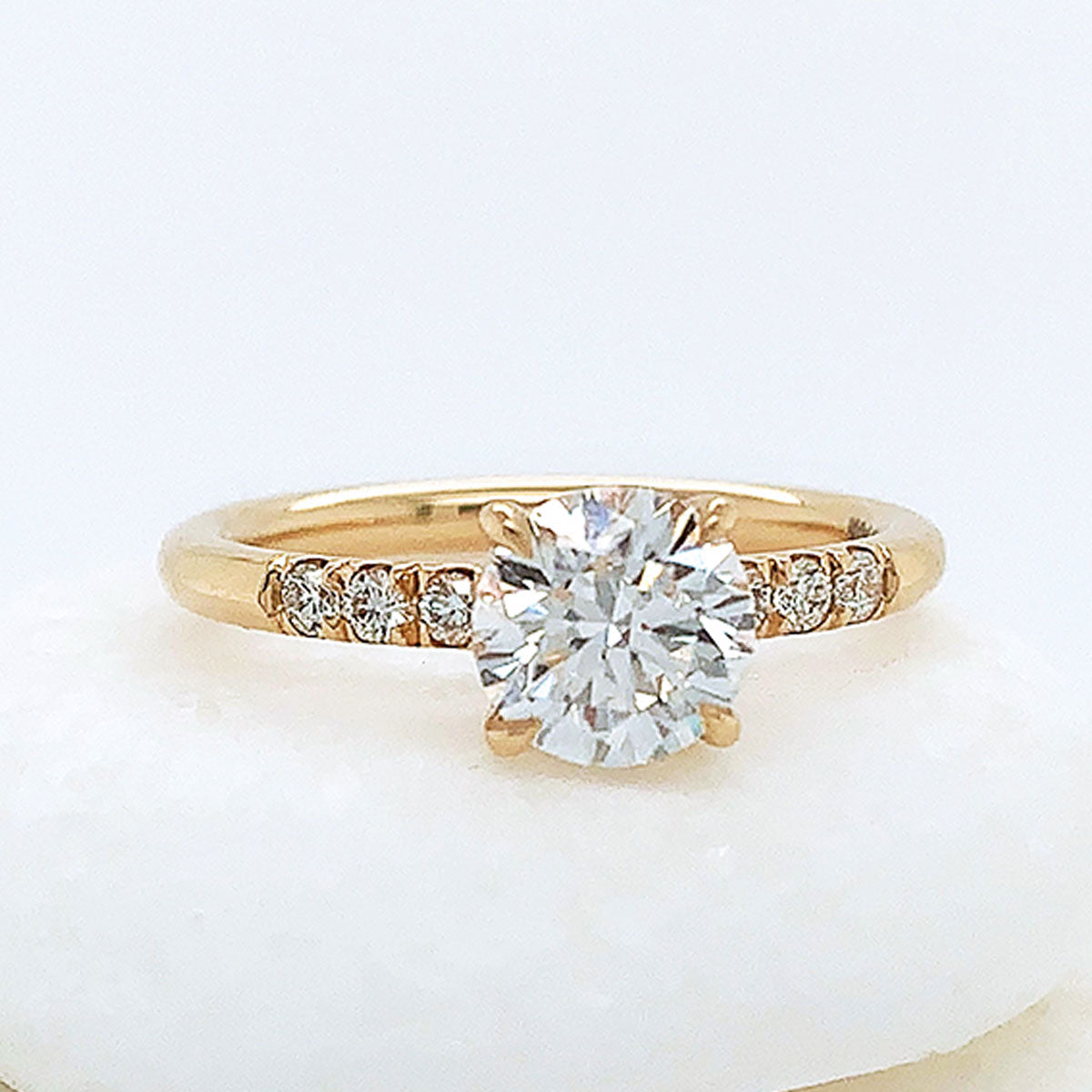 A solitaire ring with a round white diamond with 3 round white diamond stones on either side set in yellow gold on three white stones.