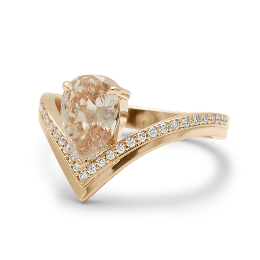 Angled view of a pear champagne diamond set on top of a chrysalis band with white diamond pave set in yellow gold.