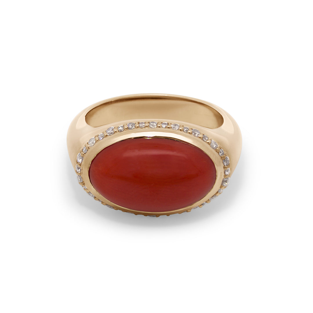 A yellow gold ring featuring a red coral cabochon center and a champagne diamond halo on a white background