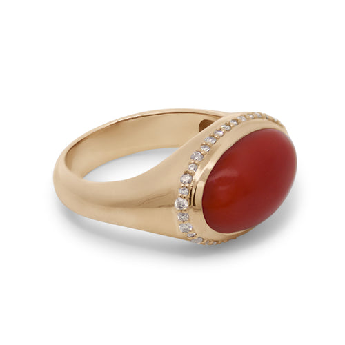 A yellow gold ring featuring a red coral cabochon center and a champagne diamond halo on a white background