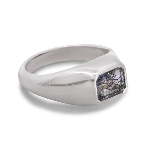 A silver ring featuring an emerald cut black and white black rutile quartz gemstone on a white background