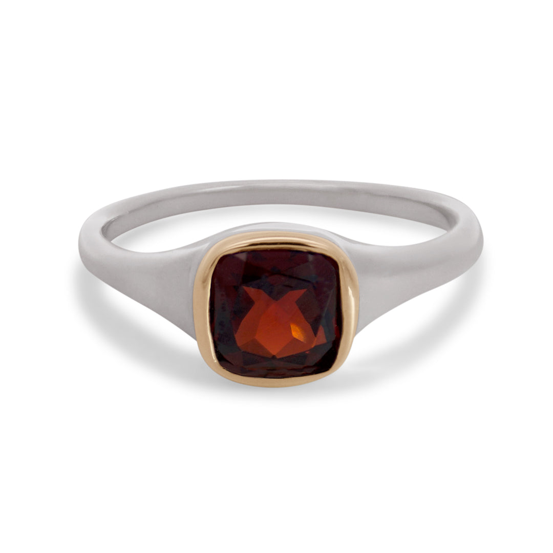 A sterling silver ring featuring a cushion cut red garnet gemstone set in a yellow gold bezel on a white background