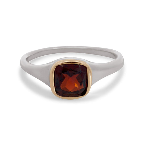 A sterling silver ring featuring a cushion cut red garnet gemstone set in a yellow gold bezel on a white background