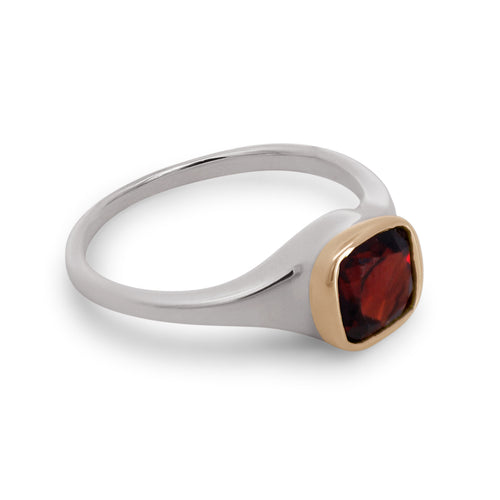 A sterling silver ring featuring a cushion cut red garnet gemstone set in a yellow gold bezel on a white background