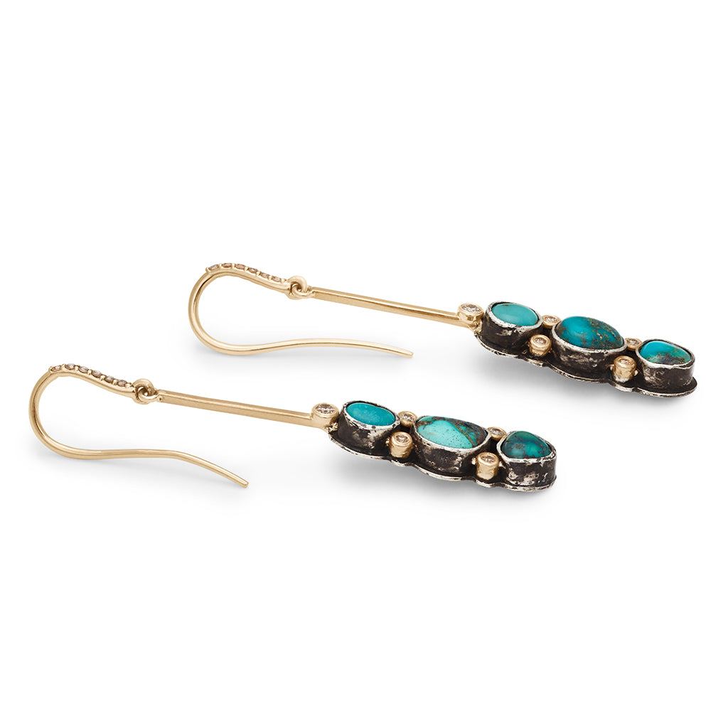Side view of a pair of drop earrings with turquoise stones set in sterling silver and champagne diamond pave accent stones and on the earwire set in yellow gold.