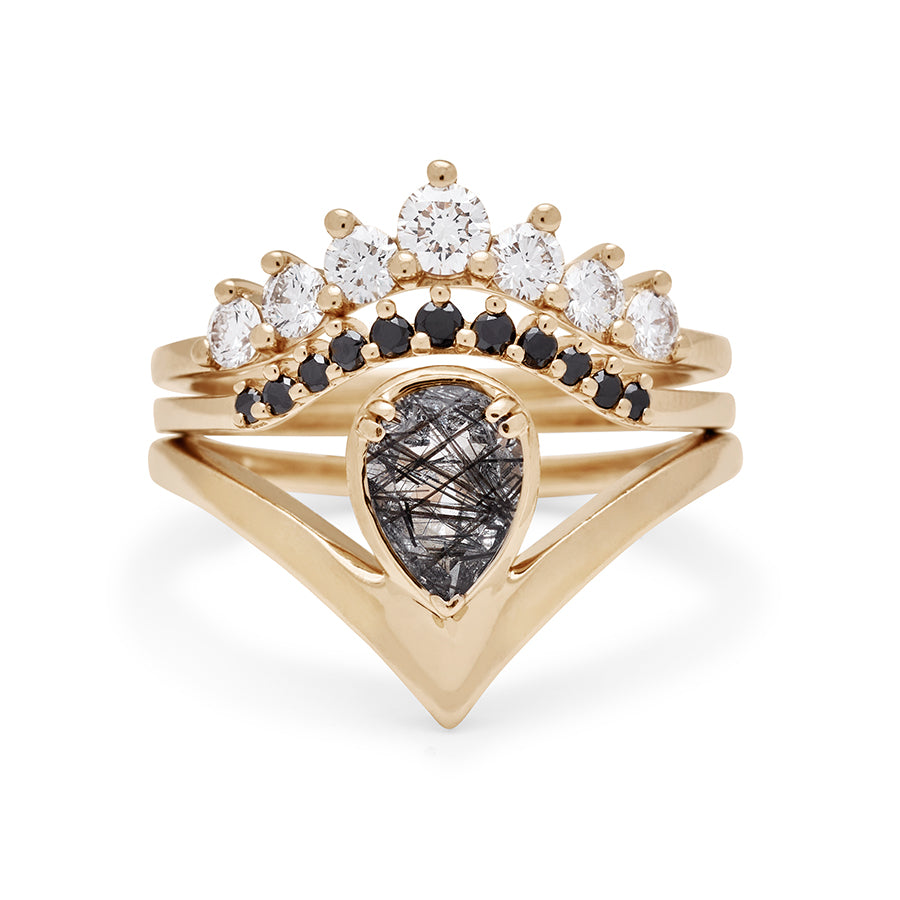A pear shaped black rutilated quartz ring set in yellow gold stacked beneath two curved nesting band one white diamond and one black diamond.