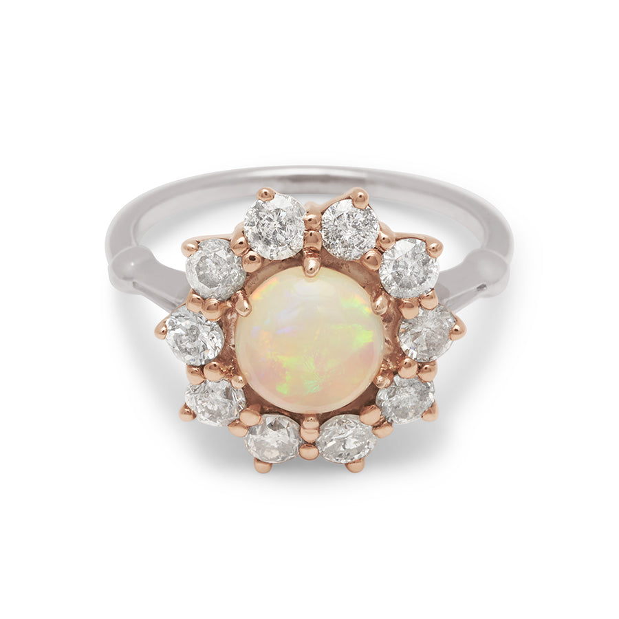 A ring with a round opal center stone surrounded by round grey diamonds set in a rose gold basket and a white gold band.