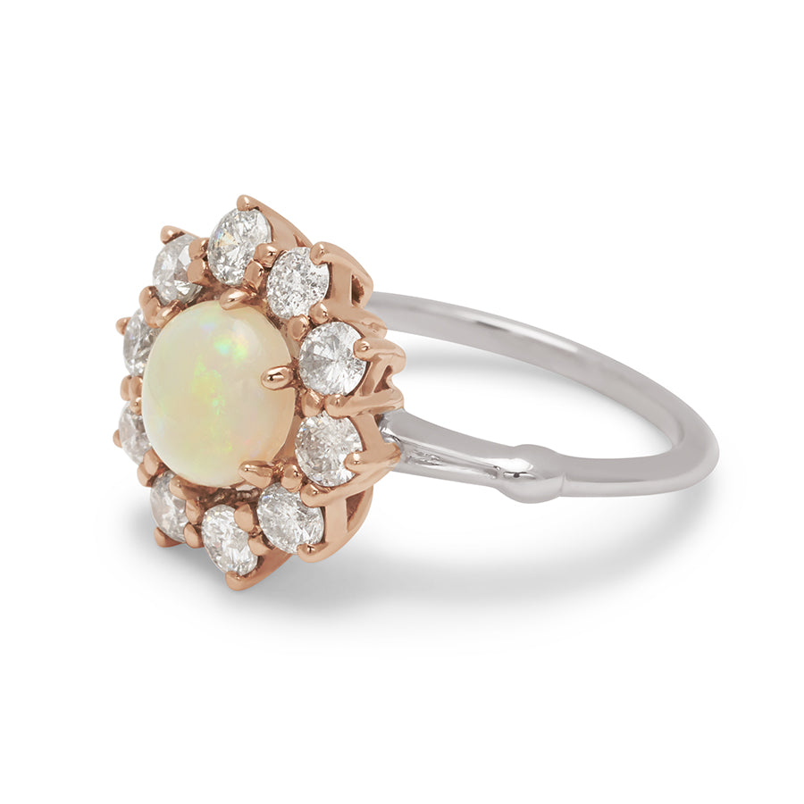 Angled view of a ring with a round opal center stone surrounded by round grey diamonds set in a rose gold basket and a white gold band.