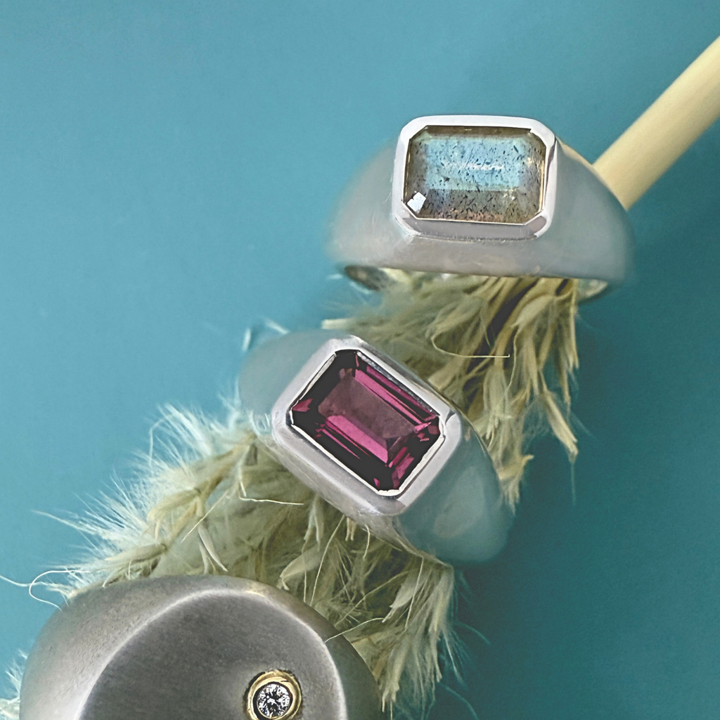 silver gemstone rings featuring pink tourmaline and labradorite on a blue paper 